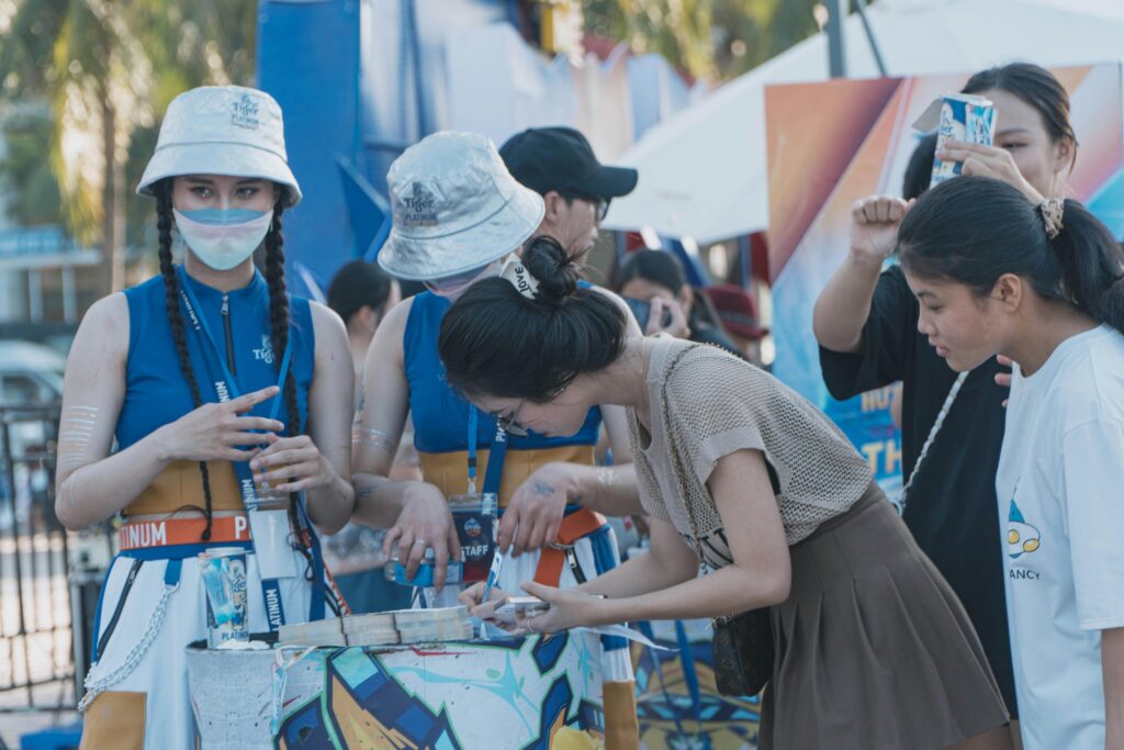 People interacting at an outdoor festival booth wearing colorful outfits and hats.