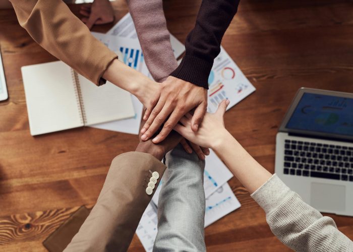 Diverse professionals unite for teamwork around a wooden table with laptops and documents.